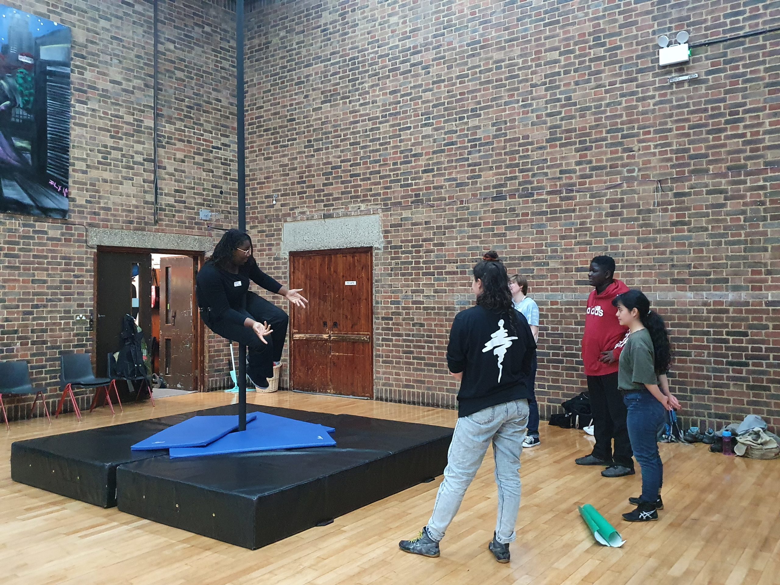 group of young people watching young aerialist demonstrate on chinese pole