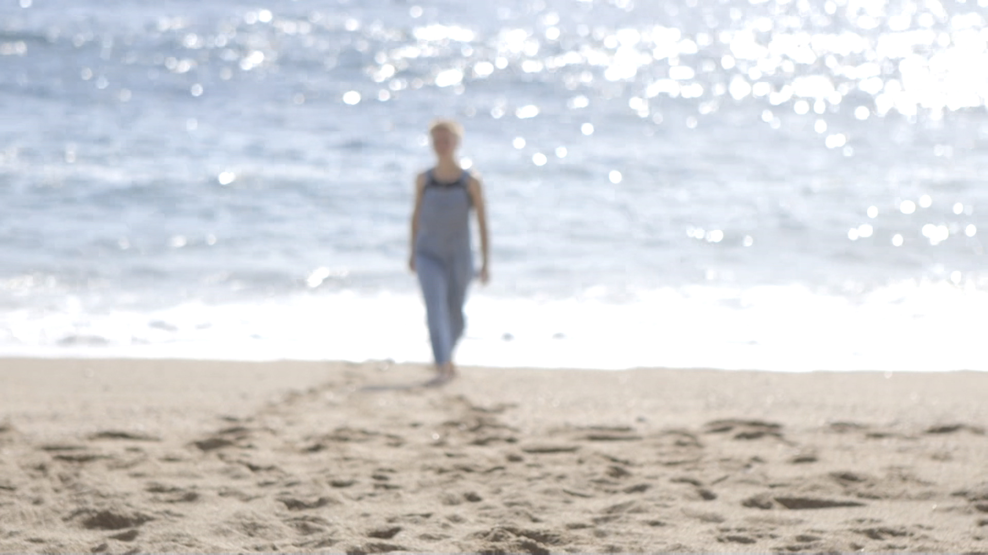 Blurred image of person in dungarees walking on beach, as if emerging from the sea.