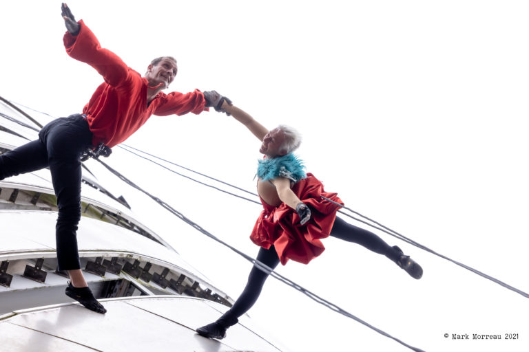 Two aerial performers suspended on ropes, jumping from the side of The Lowry building while holding hands