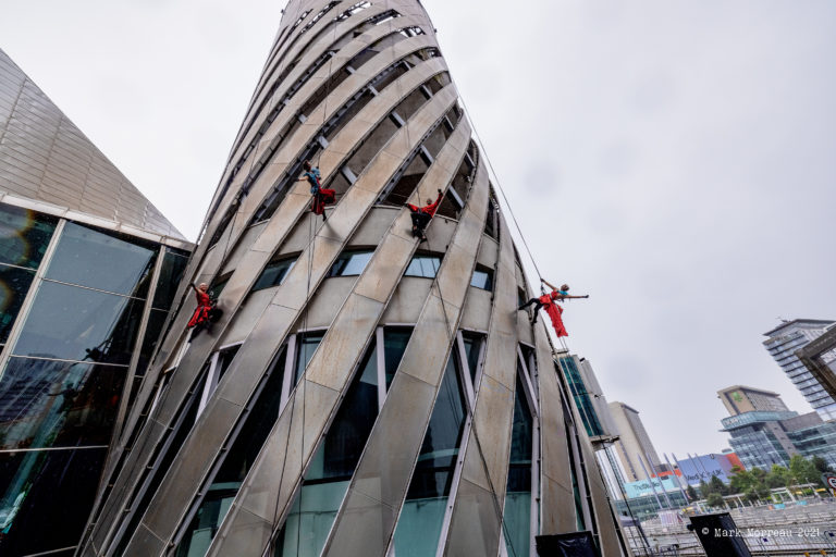 Four aerial performers suspended from top of tall building