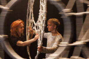 Emerging. Daniela and Naissa smile at eachother through a webbed hoop