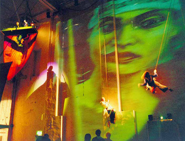 Two performers suspended in air in front of an illuminated backdrop