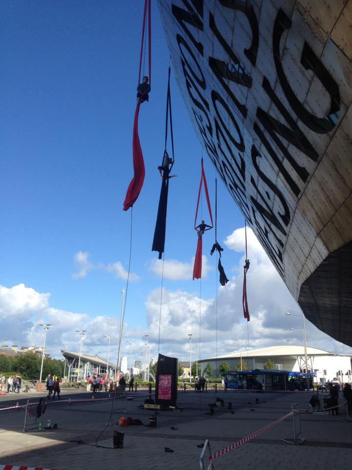 Five aerial performers suspended by slings from side of building