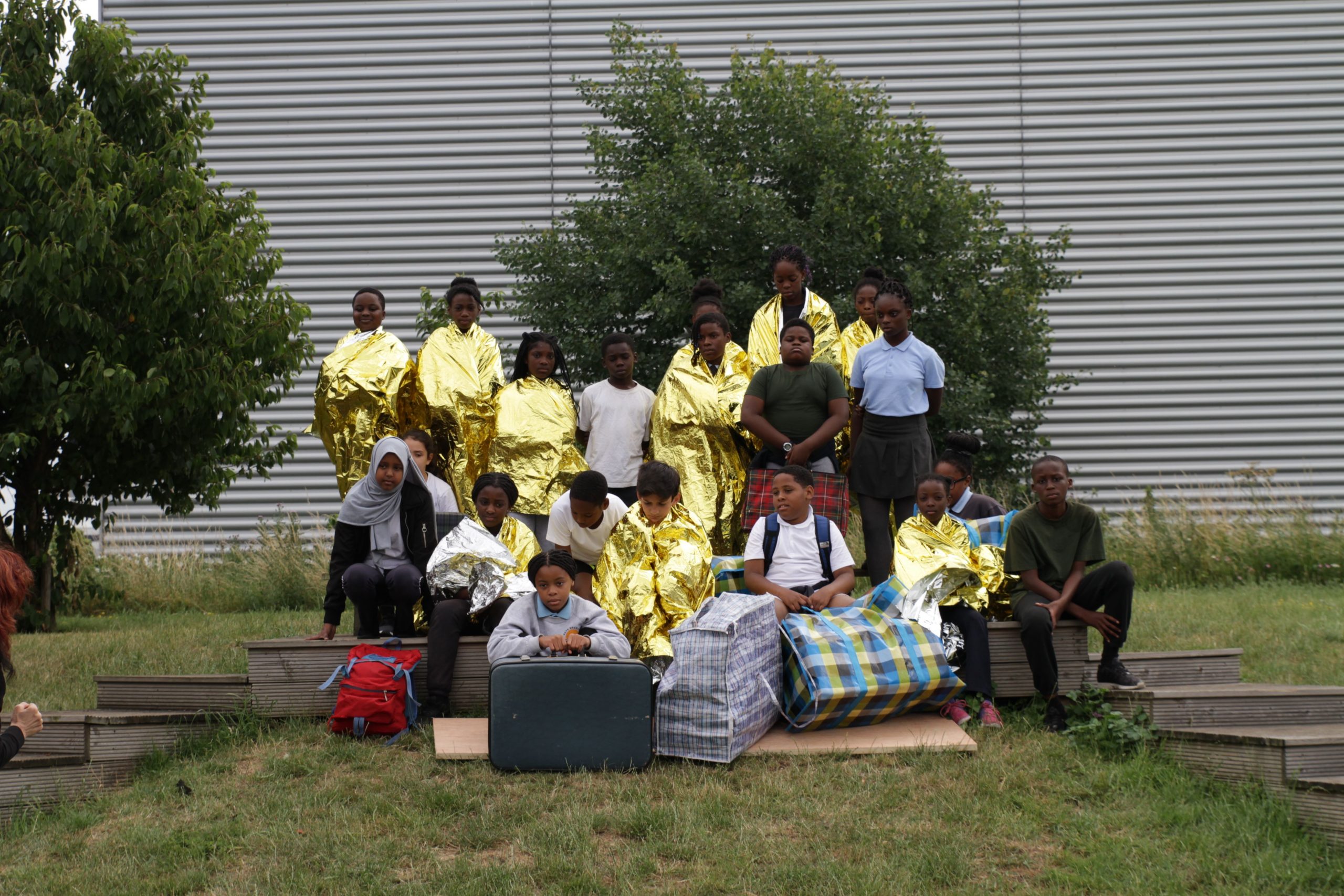 Large group of children dressed in gold raps with tartan plastic carriers