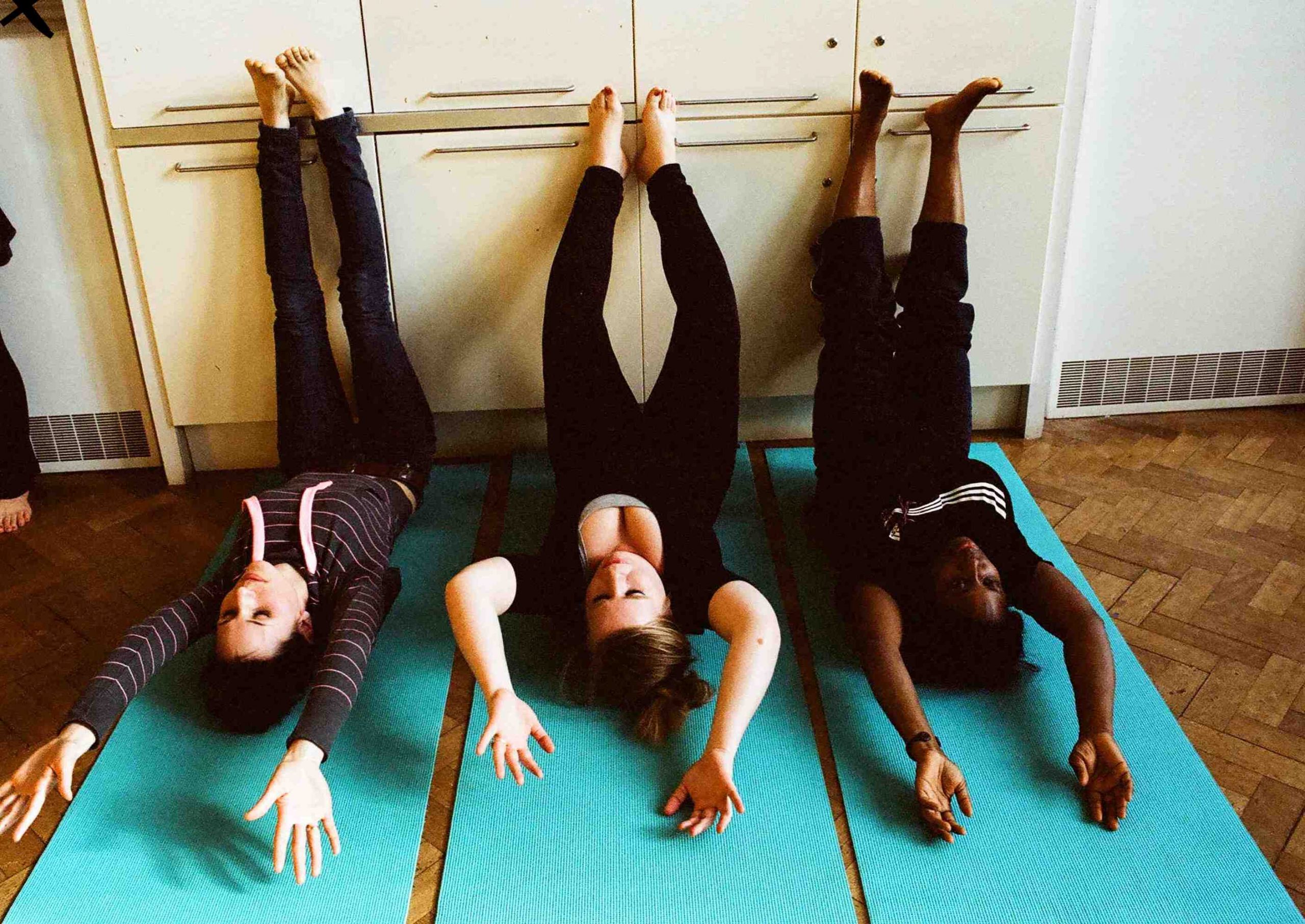 Three woman lying on their backs, arms above them, legs up resting on wall